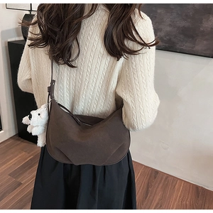 Close-up of brown suede half-moon shoulder bag featuring a cute white teddy bear pendant
