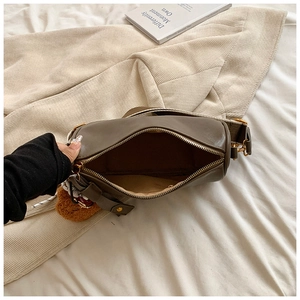 Brown Boston cylinder bag with wide woven strap and plush charm on textured fabric