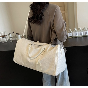 Dettaglio di una borsa da viaggio bianca intrecciata con doppi manici e tracolla rimovibile