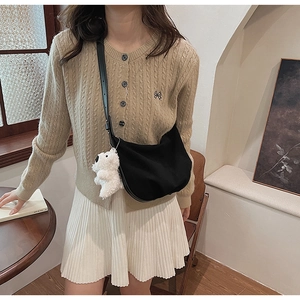 Detail of black matte hobo bag with plush bear charm styled with knit sweater and skirt