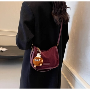 Détail du sac demi-lune en velours bordeaux avec charm monstre en peluche et métal doré