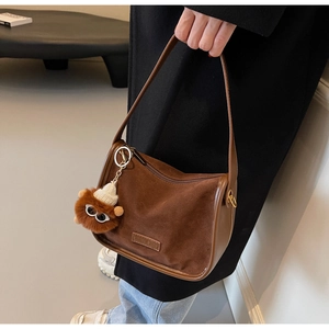 Détail du sac bandoulière vintage en daim marron avec logo et breloque en peluche