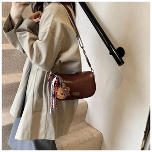 Detail of dark brown Boston bag with Fashion plaque, bear charm and woven tassel strap