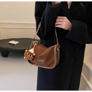 Détail du sac demi-lune en daim marron avec bordure en cuir et breloque lion en peluche