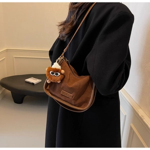 Gros plan du sac bandoulière en daim marron avec pendentif en peluche et logo cuir