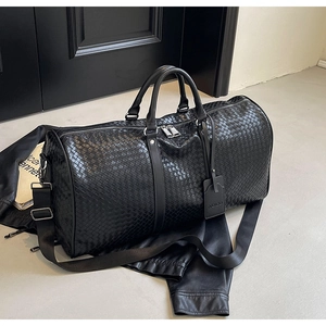 Dettaglio della trama in pelle intrecciata nera e finiture metalliche della borsa da viaggio