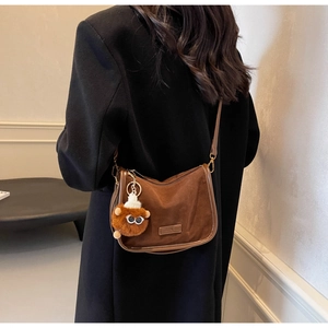 Vue détaillée du sac bandoulière en daim marron avec charm monstre en peluche et bordure