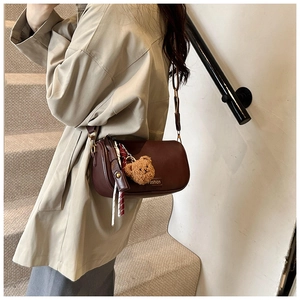 Detail of dark brown Boston bag featuring teddy bear charm and woven ribbon accessory