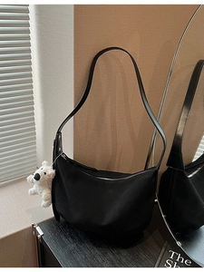Minimalist black crescent shoulder bag with white plush bear charm on a wooden table