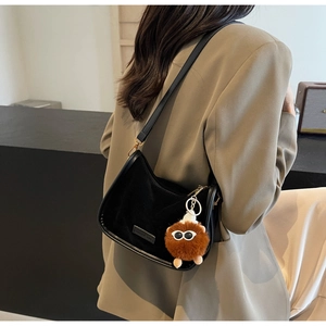 Détail du sac hobo en daim noir avec un pendentif monstre en peluche marron sur la bandoulière