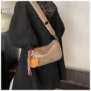 Detail of khaki Boston bag with wide fabric strap, featuring bear charm and fashion plaque