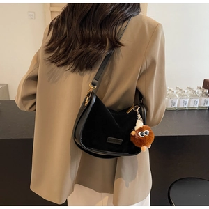 Détail du sac hobo noir avec un charme en peluche et des finitions dorées sur modèle