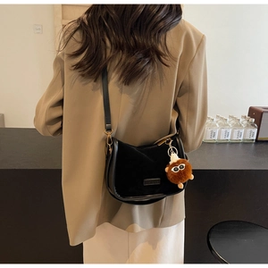 Détail d'un sac besace noir vintage avec breloque en peluche porté par un mannequin chic