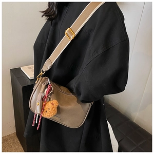 Detail view of khaki half-moon shoulder bag with plush bear charm and wide fabric strap