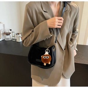 Détail d'un sac bandoulière demi-lune noir avec un charmant monstre en peluche marron