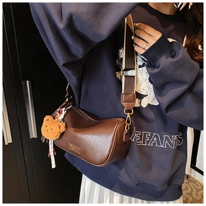 Detail of brown PU leather Boston bag with wide woven strap and plush bear charm