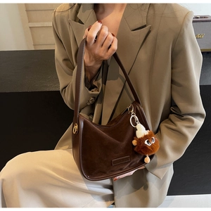 Vue détaillée du sac demi-lune en daim marron foncé avec breloque peluche et bijoux dorés
