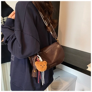 Detail view of a dark brown crescent hobo bag with wide patterned strap and plush bear charm