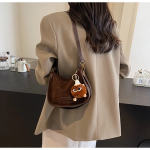 Détail d'un sac demi-lune en daim marron foncé avec un pendentif monstre en peluche