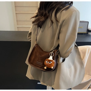 Vue latérale d'un sac demi-lune en daim marron avec un joli pendentif peluche