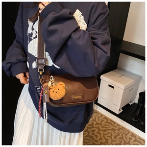 Detail of dark brown vintage Boston crossbody bag with wide canvas strap and bear charm