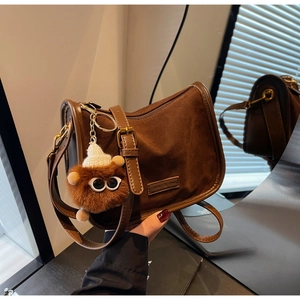 Détail du sac bandoulière en daim marron avec un charme monstre en peluche et sa lanière