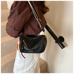 Detail of black glossy Boston bag with fashion plaque, stripe strap and plush charm