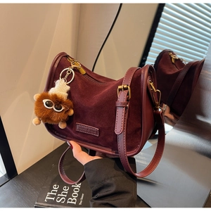 Gros plan du sac bandoulière vintage en daim bordeaux avec matériel rétro et breloque