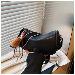 Detail view of a black leather Boston bag with a wide strap and plush pom-pom charm