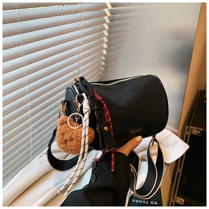 Close-up of black leather Boston bag with teddy bear charm and wide striped shoulder strap