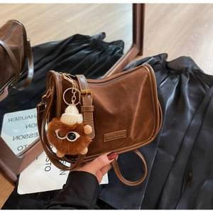 Détail du sac baguette en daim marron avec bandoulière réglable et breloque en peluche