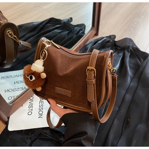 Détail du sac bandoulière en daim marron foncé avec logo et breloque en peluche