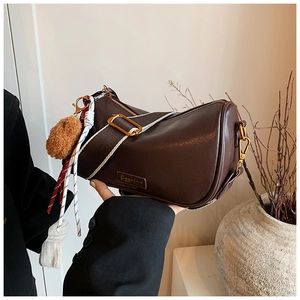 Detail of a dark brown Boston bag with a wide woven strap and golden zipper hardware