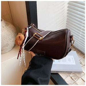 Close-up of brown Boston bag with wide fabric strap and plush bear charm detail