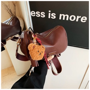 Detail of a dark reddish-brown Boston pillow bag with bear charm and fashion nameplate