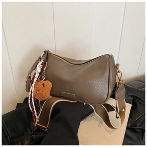 Detail view of taupe half-moon shoulder bag with plush bear charm and woven strap