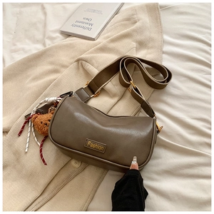 Detail view of coffee Boston bag featuring Fashion plaque, wide strap, and plush bear charm