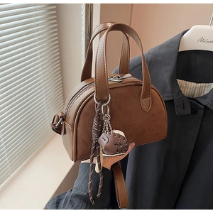 Detail van een bruine crossbodytas met decoratieve hangers en lederen handgrepen