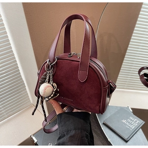 Detail van bordeauxrode lederen en suède crossbodytas met honkbalbedel en gouden ritsen