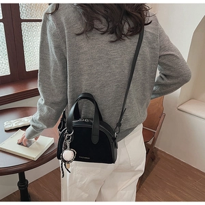 Zwarte ronde crossbodytas met baseballhanger getoond in een stijlvolle lifestyle-omgeving