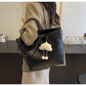 Detail of black leather tote bag featuring white contrast stitching and plush cloud charm