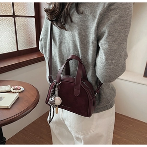 Detail van bordeauxrode crossbodytas met matte textuur en decoratieve honkbalbedel