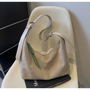 Detail of beige suede bucket bag featuring adjustable leather strap and green woven tassel