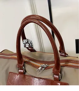 Detail of the reinforced leather handles and dual metal zippers on a khaki travel bag