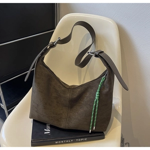 Detail of dark brown suede bucket bag with unique green braided rope charm on the side