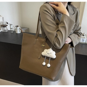 Close-up of brown faux leather tote with white stitching and plush cloud pendant