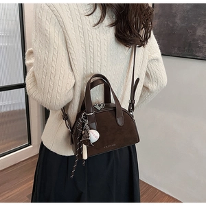 Detail van koffiekleurige crossbodytas met honkbalbedeltje op beige gebreide trui