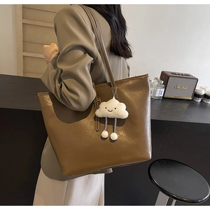 Large brown leather tote bag with a cute cloud charm shown on a shoulder in a modern room