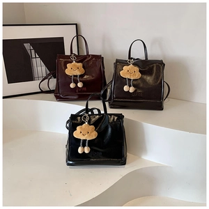 Close-up of glossy leather backpacks in burgundy and black with plush cloud charms