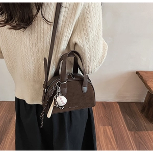 Detail van donkerbruine suède crossbodytas met honkbalhanger en merklogo-opdruk